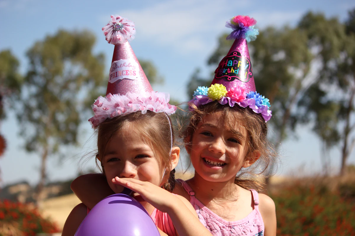 Zwei Mädchen mit bunten Partyhütchen lachen auf einem Kindergeburtstag